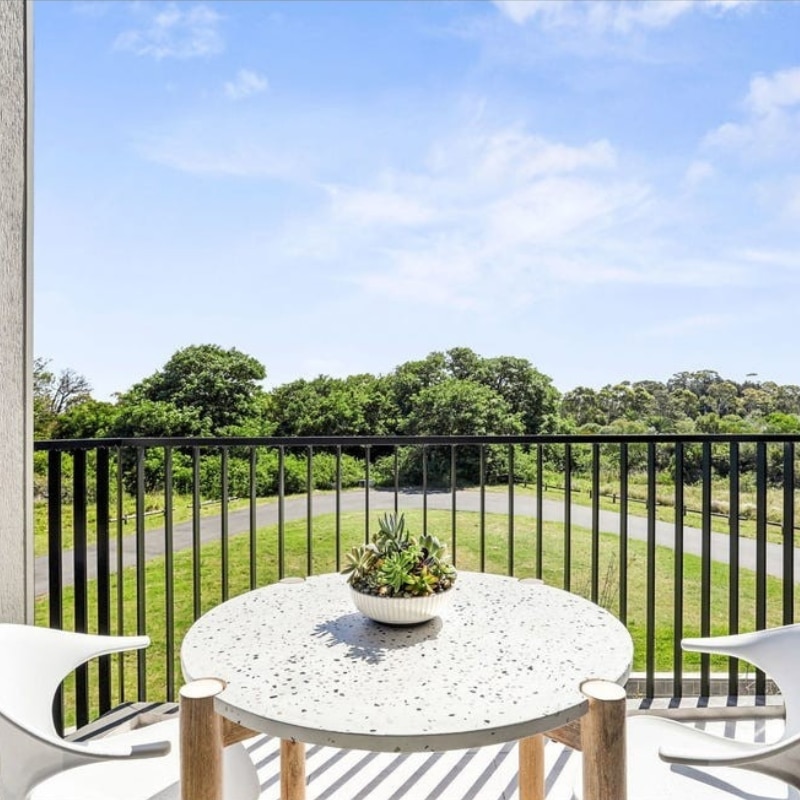 Two white chairs with a round coffee table set outside a modern duplex at 55 Eyre Street, Chifley, 2036 — ideal for enjoying the weather.
