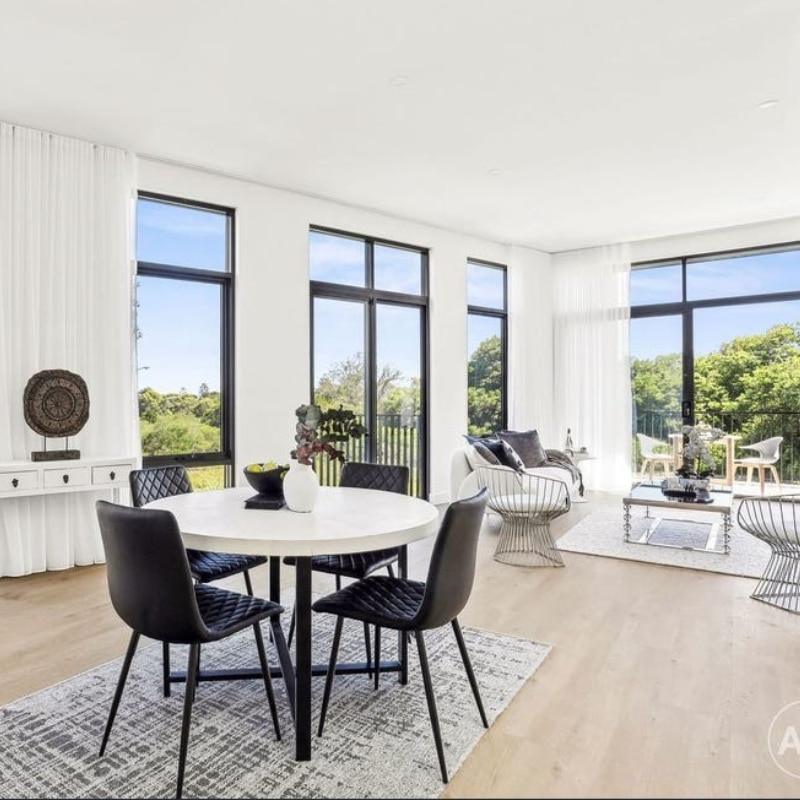 Modern dining area with a round table, black chairs, large windows, and a view of greenery at 55 Eyre Street, Chifley, 2036 – Duplex, creating a bright and airy atmosphere.