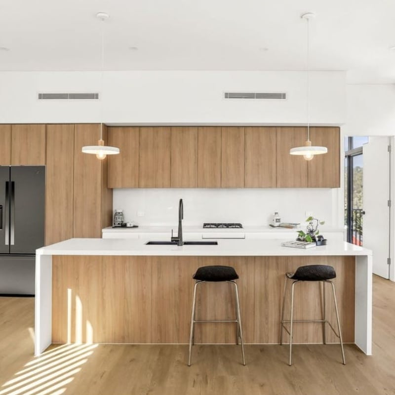 Modern kitchen at 55 Eyre Street, Chifley, 2036-Duplex featuring sleek white countertops, wooden cabinetry, stainless steel appliances, and stylish bar stools. Bright and inviting space.