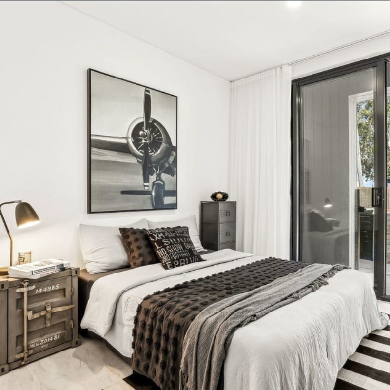 Cosy bed with white and black pillows in a minimalist-style duplex bedroom with black and white wall paint at 55 Eyre Street, Chifley, 2036.