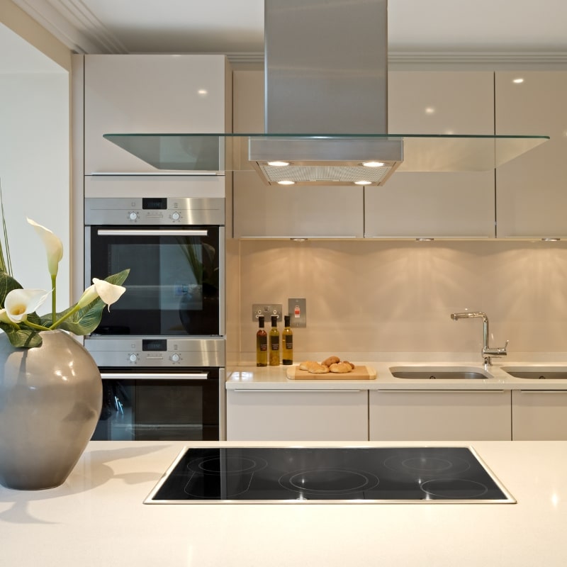 Crafting Quality Homes with Integrity & Precision – Modern kitchen with sleek cooktop, glass hood, stylish appliances, flowers in a vase, and fresh bread on a cutting board