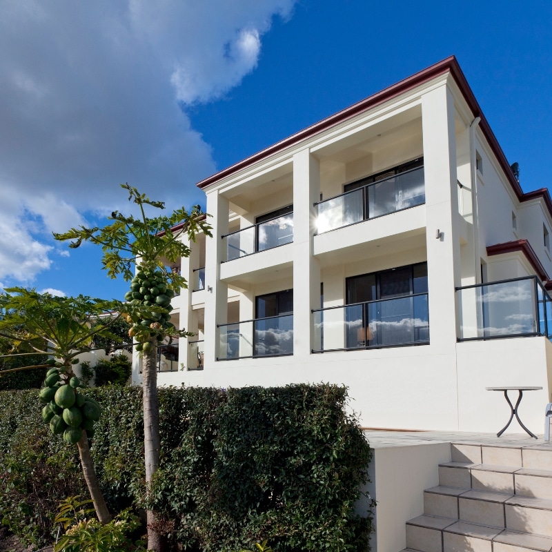 Double Storey Home Builders Sydney – Modern two-storey home with brown tiled roof, beige exterior, green shutters, wooden front door, and attached garage