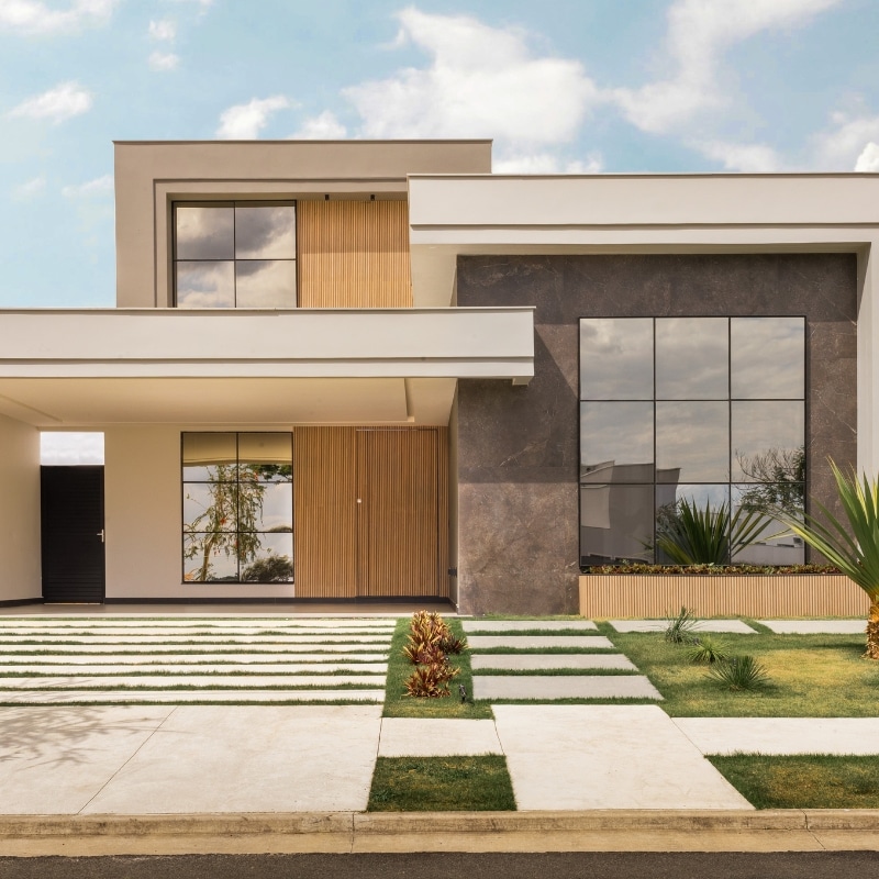 Duplex. – Modern two-storey home with large windows, wooden accents, stone pathways, and landscaped greenery