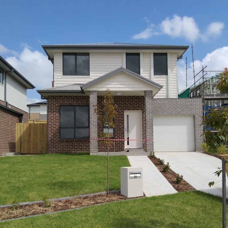 Two-storey home in Leppington, featuring brown brickwork with grey and white painted accents and a large landscaped front yard.