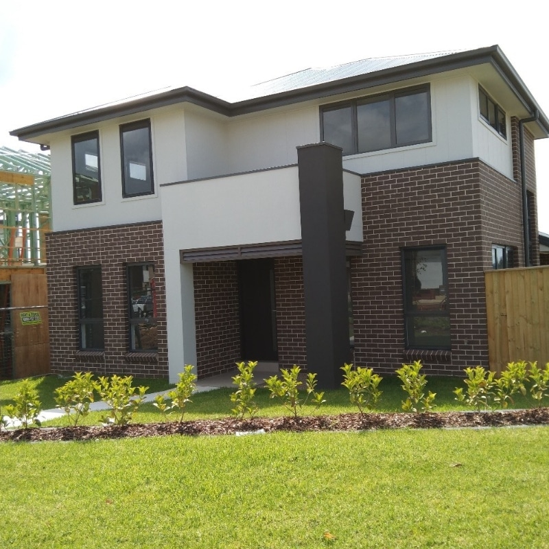 Side view of a two-storey house in Leppington featuring brown brickwork with grey and white painted finishes and a spacious landscaped yard.