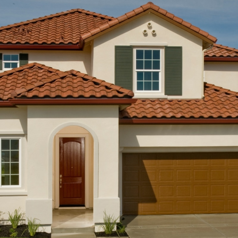 Why Choose Sydney East Building & Renovation – Two-storey home with terracotta tile roof, brown front door, green shutters, two-car garage, and minimal landscaping