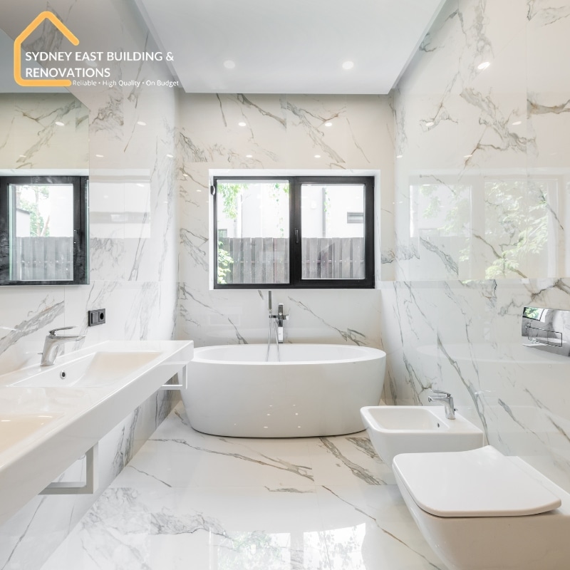 Bathroom Renovations in Malabar showcasing a modern bathroom with marble walls, freestanding tub, sleek sink, and natural light.