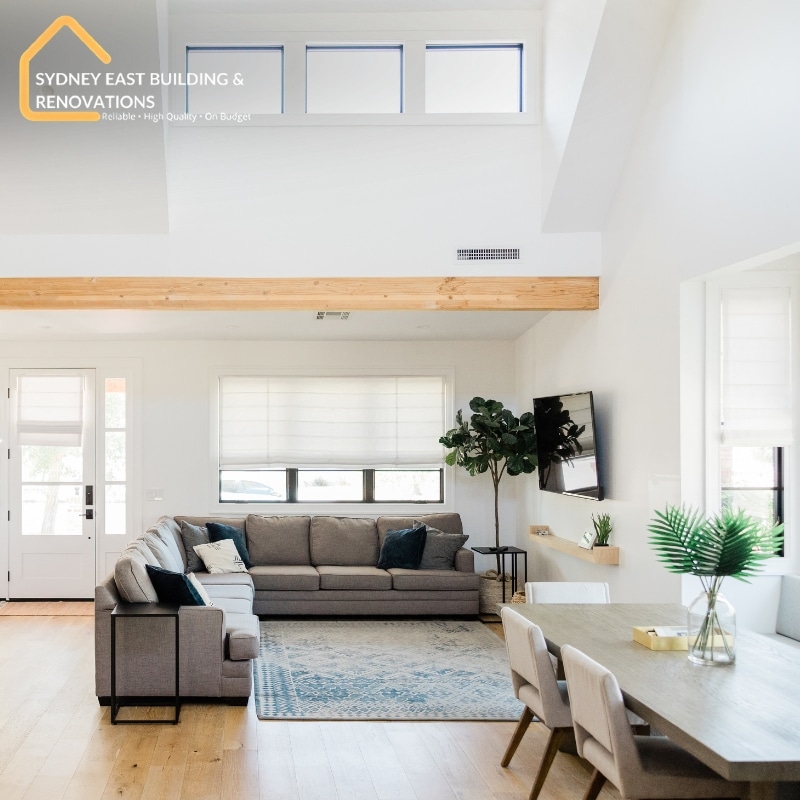 Home Renovation in Waverley featuring a modern living room with a grey sofa, dining table, wood accents, plants, and natural light.