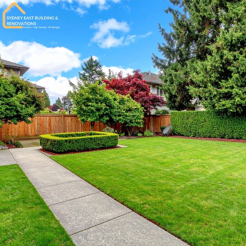Beautiful backyard designed by a Sydney landscaping company featuring manicured lawn, lush hedges, trees, and a stone pathway.